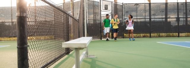 Three young kids walking on the tennis court
